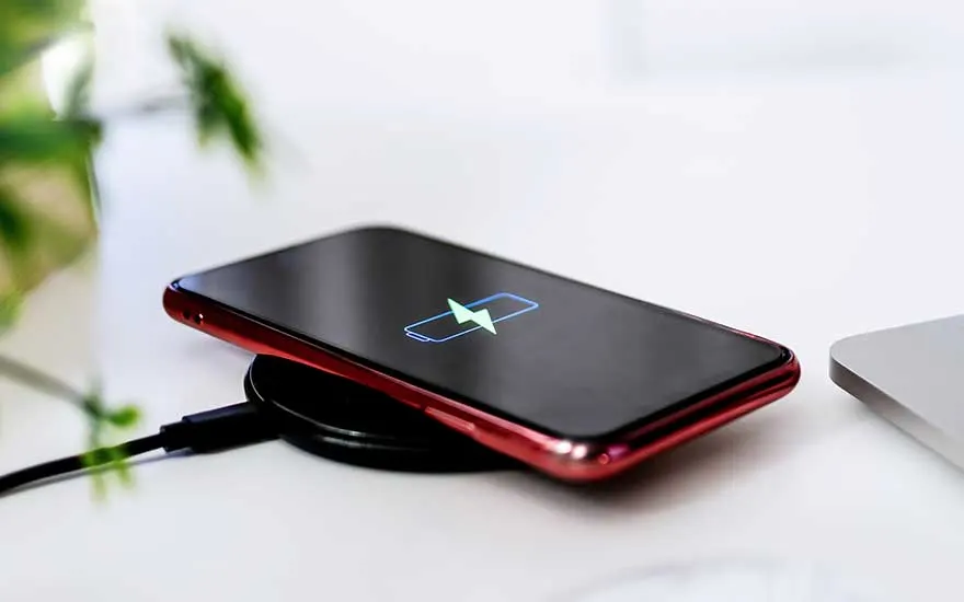 Un téléphone rouge se charge sans fil sur un chargeur noir. Un symbole de batterie apparaît sur l'écran noir.