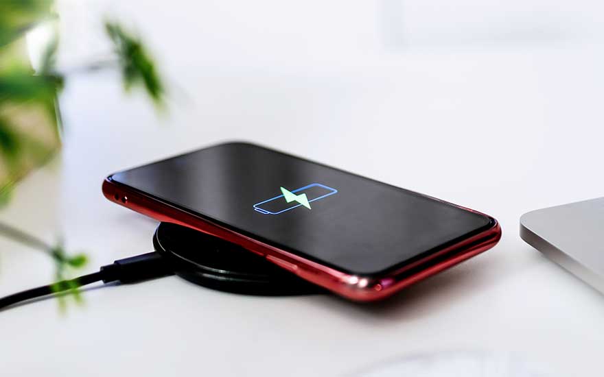 Un téléphone rouge se charge sans fil sur un chargeur noir. Un symbole de batterie apparaît sur l'écran noir.