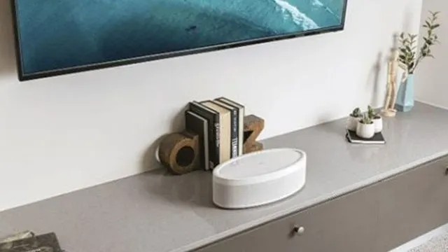 Een tv boven een grijs dressoir met decoraties zoals boeken, planten en een witte luidspreker.