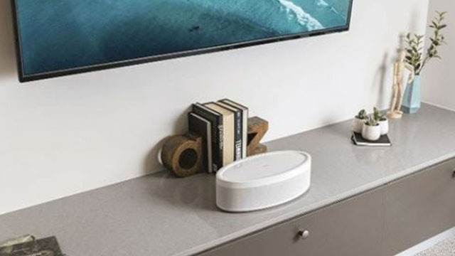 Téléviseur mural au-dessus d'une commode grise avec haut-parleur blanc, livres, serre-livres et petites plantes.