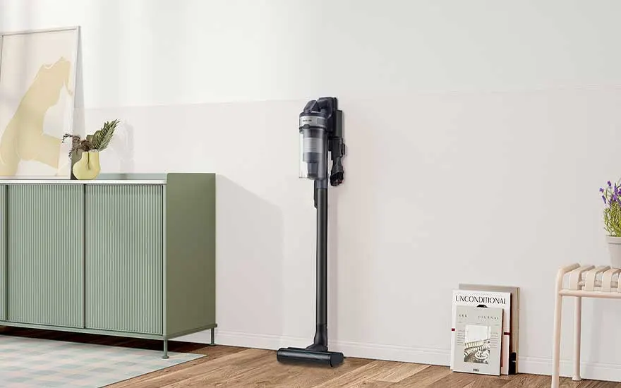 Donkergrijze steelstofzuiger hangt strak aan de wand in een lichte kamer, naast groen dressoir en decoratieve tijdschriften op de vloer.