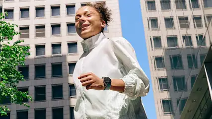 Une personne en veste blanche court devant des immeubles de bureaux par une journée ensoleillée.