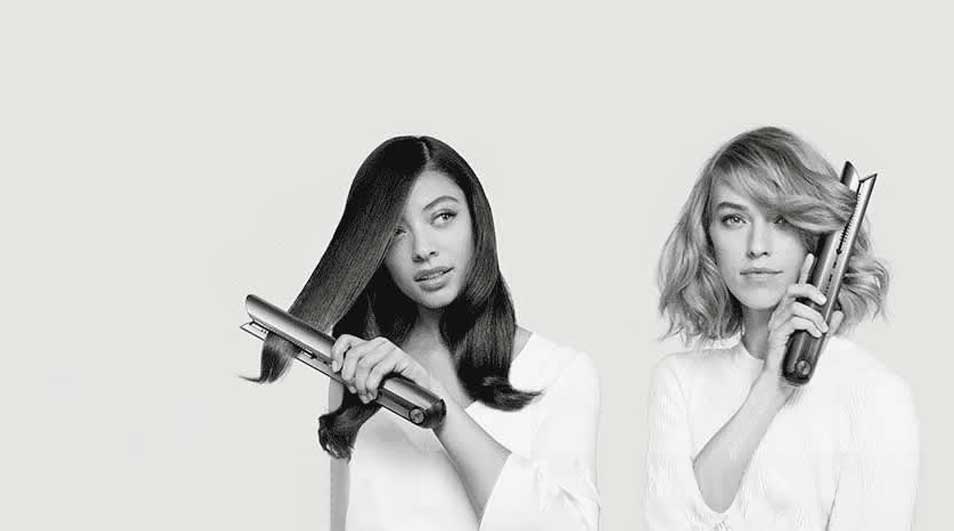 Deux personnes utilisent des fers à lisser sur fond blanc. L'une lisse ses cheveux, l'autre tient un fer fermé.