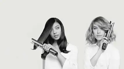 Deux personnes utilisent des fers à lisser sur fond blanc. L'une lisse ses cheveux, l'autre tient un fer fermé.