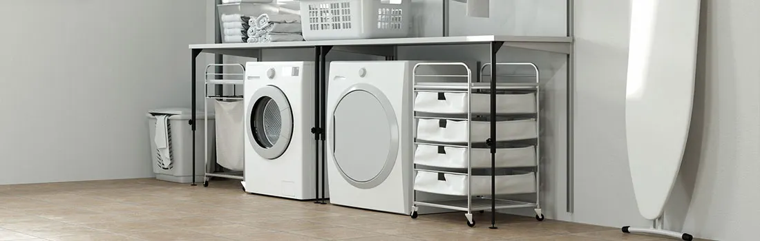 Laundry room with white washer, dryer, ironing board, storage shelves, baskets, and hampers on a brown tiled floor.