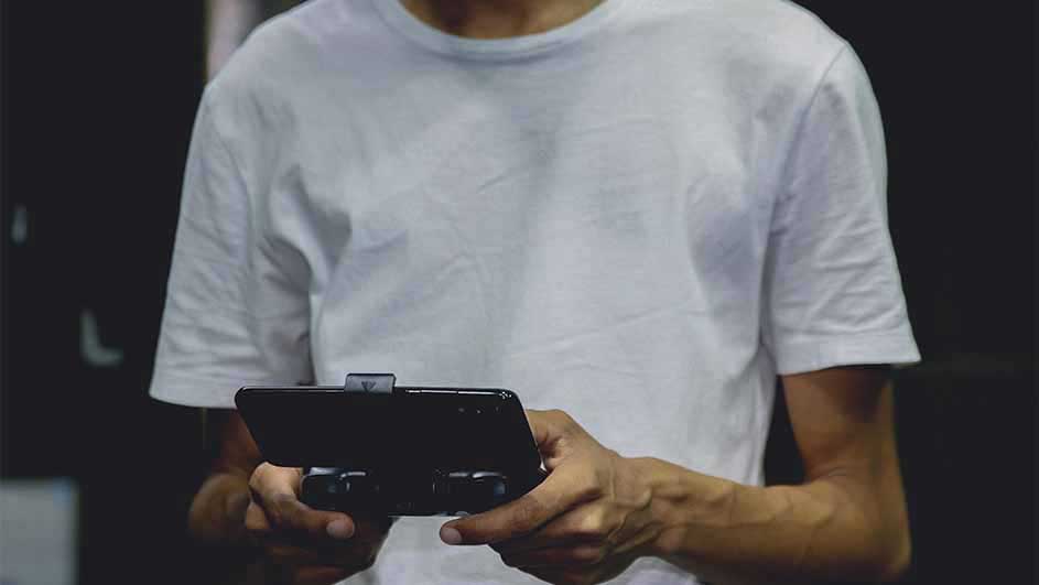 Een persoon in een wit t-shirt houdt een zwarte smartphone met een bevestigde controller vast tegen een donkere achtergrond.