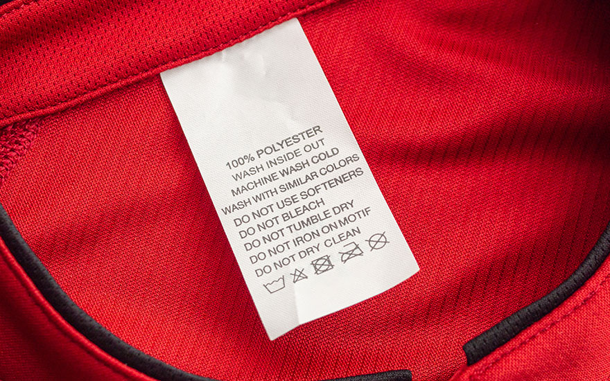 Rode stof met waslabel. Label toont instructies: 100% polyester, koud wassen, geen wasverzachter, niet bleken, niet in de droger, niet strijken, niet chemisch reinigen.