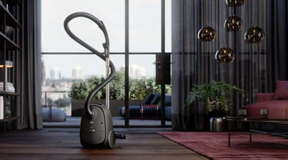A grey vacuum cleaner stands on a wood floor in a room. There is a window and city view.