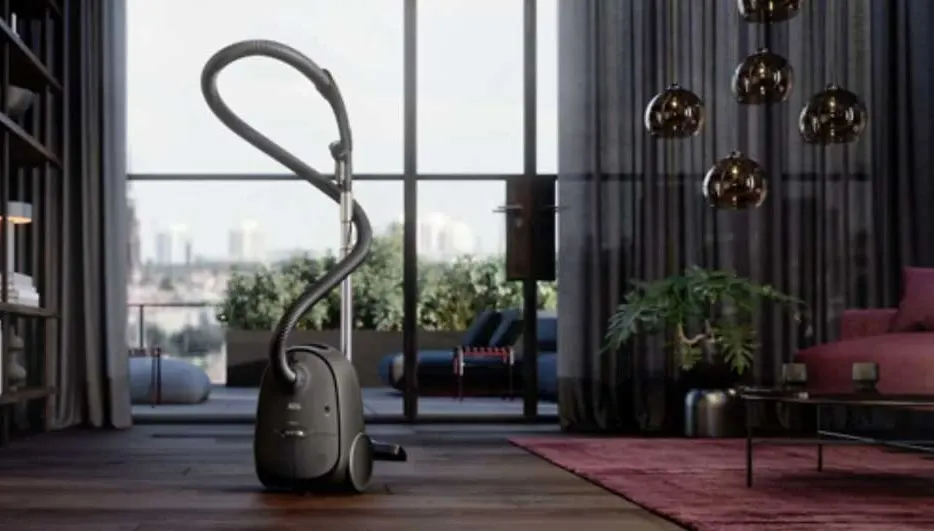 A grey vacuum cleaner stands on a wood floor in a room. There is a window and city view.