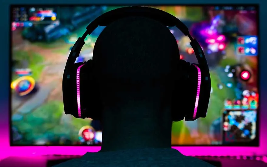 Casque audio noir avec éclairage rose devant un écran affichant un jeu vidéo coloré.