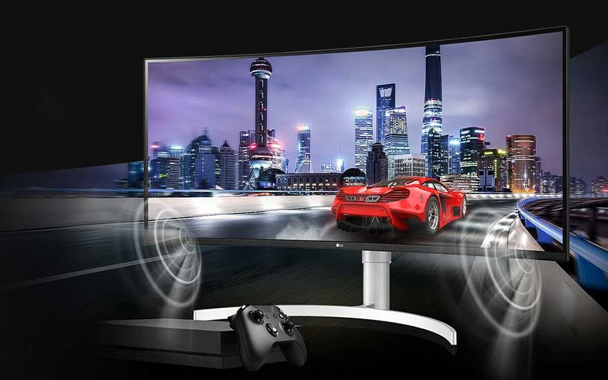 Een gebogen scherm toont een rode auto in een stadsrace, een zwarte console en controller liggen ervoor.