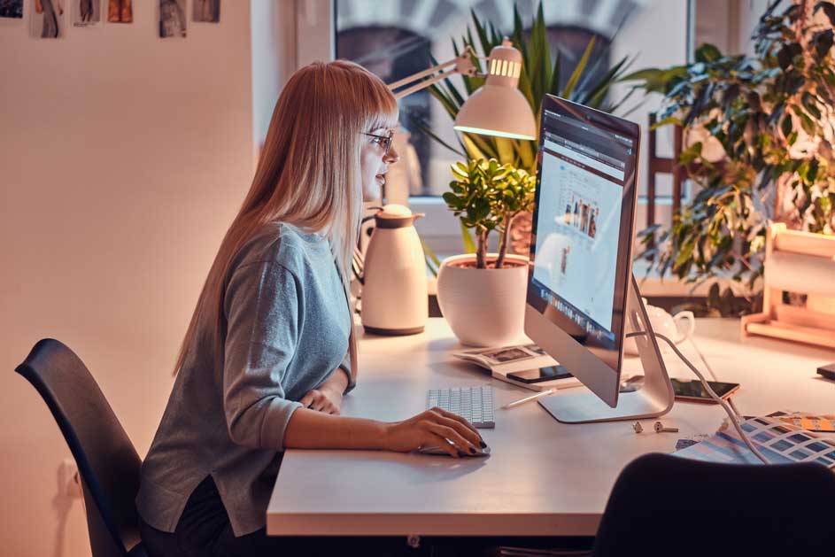 Een bureau met een computer, toetsenbord, muis, planten en een witte thermoskan. Er staat een lamp op het bureau.