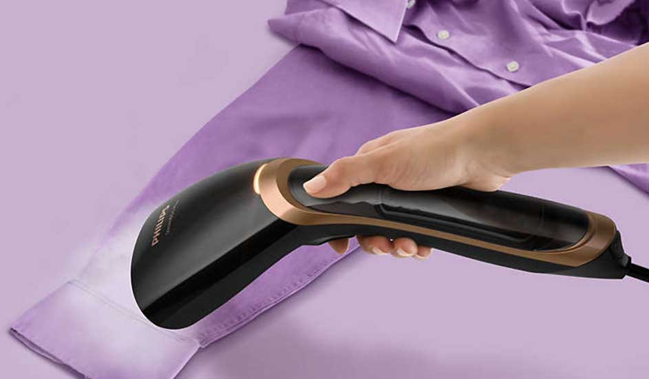Un fer à vapeur noir et or est utilisé sur une chemise violette, dégageant de la vapeur.