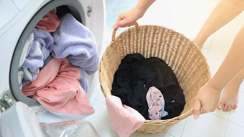 Une machine à laver pleine de linge coloré et un panier en osier rempli de vêtements noirs et roses.