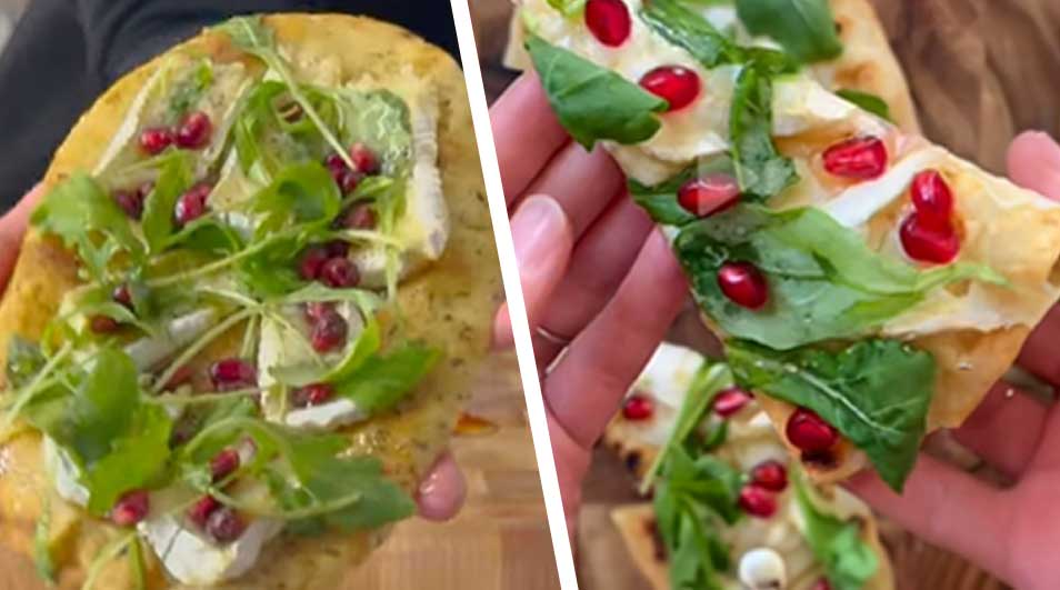 Twee stukken platbrood met rucola, granaatappelpitjes en stukjes witte kaas worden vastgehouden tegen een houten achtergrond.