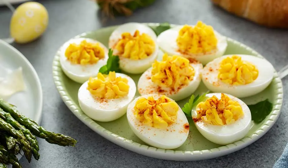 Een groen bord met gevulde eieren met een gele vulling, besprenkeld met paprika, en groene asperges.