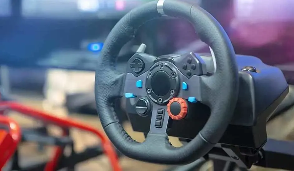 Een zwart stuurwiel met blauwe en oranje knoppen, gemonteerd op een rode race-simulator, tegen een vage achtergrond.