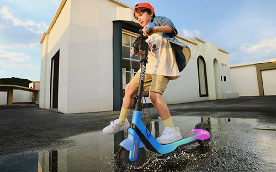 Een helm dragende rijder stuurt een robuuste elektrische step door een stoffig woestijnlandschap met bergen op de achtergrond.