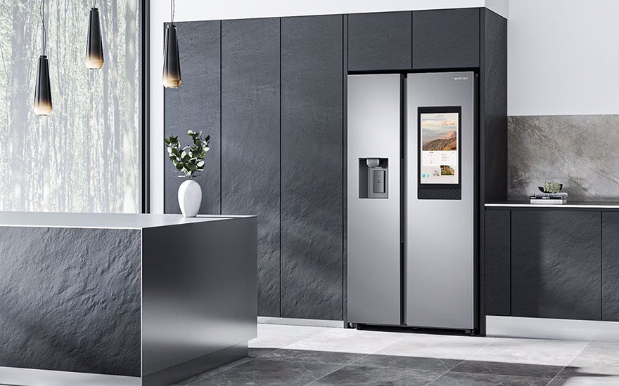 Cuisine moderne avec réfrigérateur gris à écran, îlot central et armoires anthracite. Lampes suspendues au-dessus.