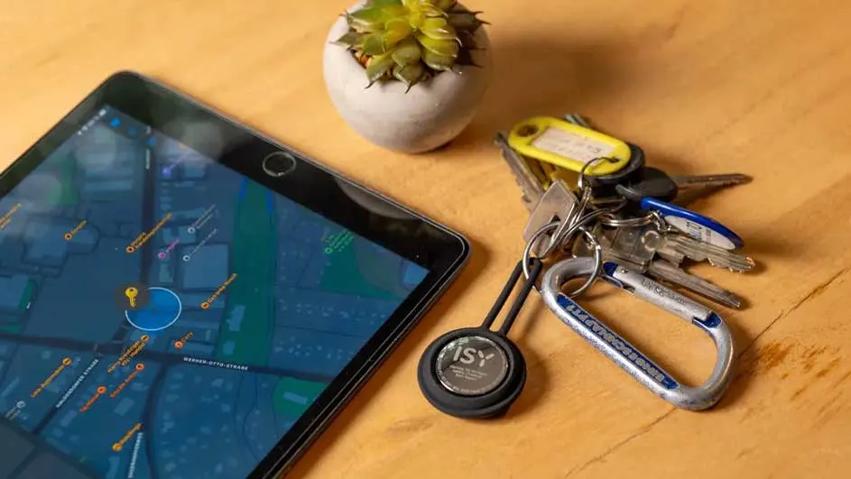 Een tablet met een kaart, sleutels aan een ring en een plant op een houten tafel.