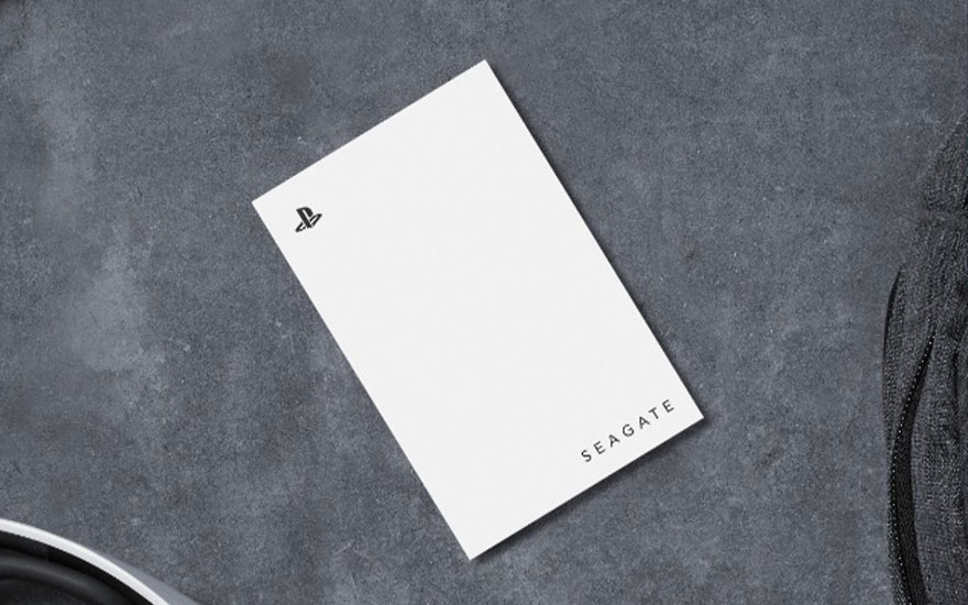 Een witte Seagate externe harde schijf met PlayStation-logo ligt op een grijze tafel, omringd door een controller en een headset.