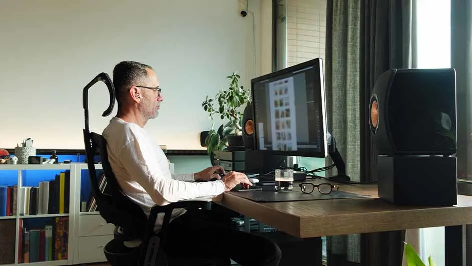 Un homme travaille à un bureau avec un ordinateur devant lui, il porte des lunettes.