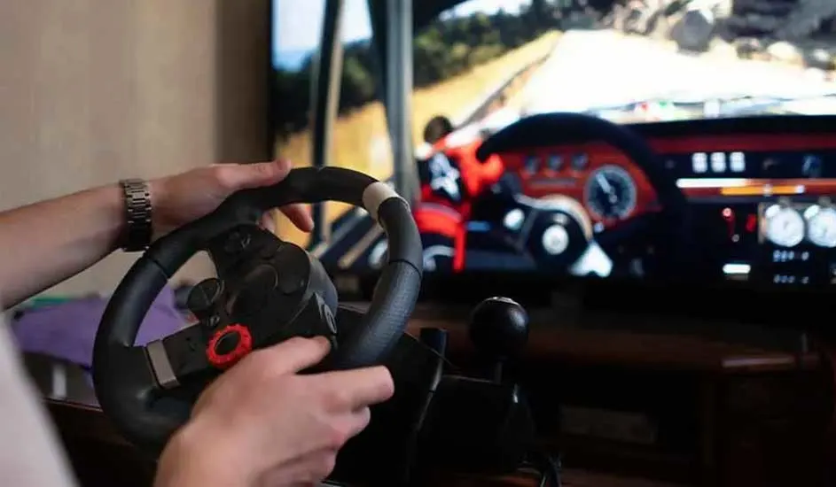 Een persoon gebruikt een zwart stuur met versnellingspook voor een tv-scherm waarop een autorace te zien is.