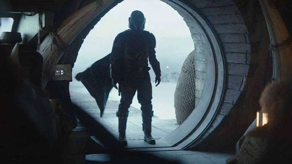 Een figuur staat in een ronde deuropening met zicht op een besneeuwd landschap, gezien vanuit een donker interieur.