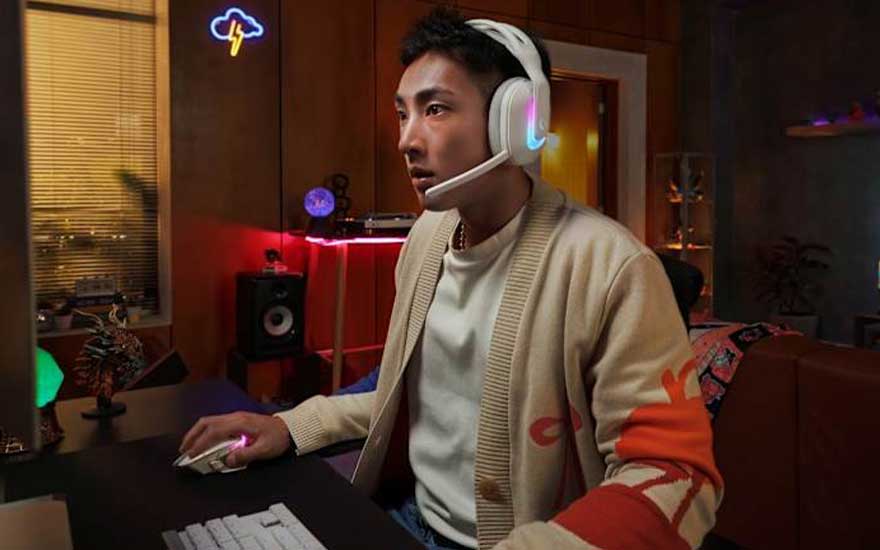 Een man draagt een witte gaming headset met microfoon terwijl hij aan een bureau zit in een modern kantoor met kleurrijke verlichting.
