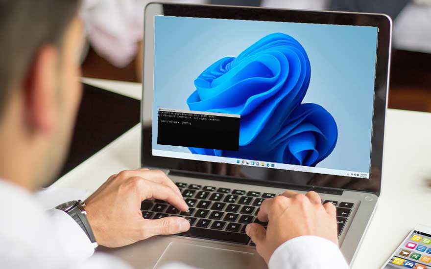 Un ordinateur portable affiche un fond d'écran bleu avec une fenêtre de commande ouverte, sur une table blanche à côté d'un téléphone.