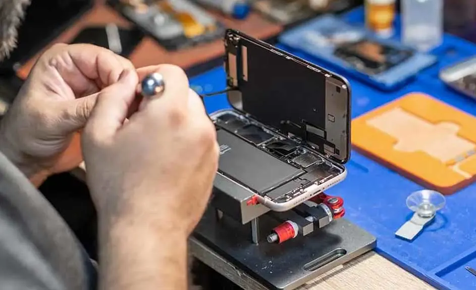 Un téléphone ouvert est réparé avec un outil sur une surface bleue avec d'autres outils.