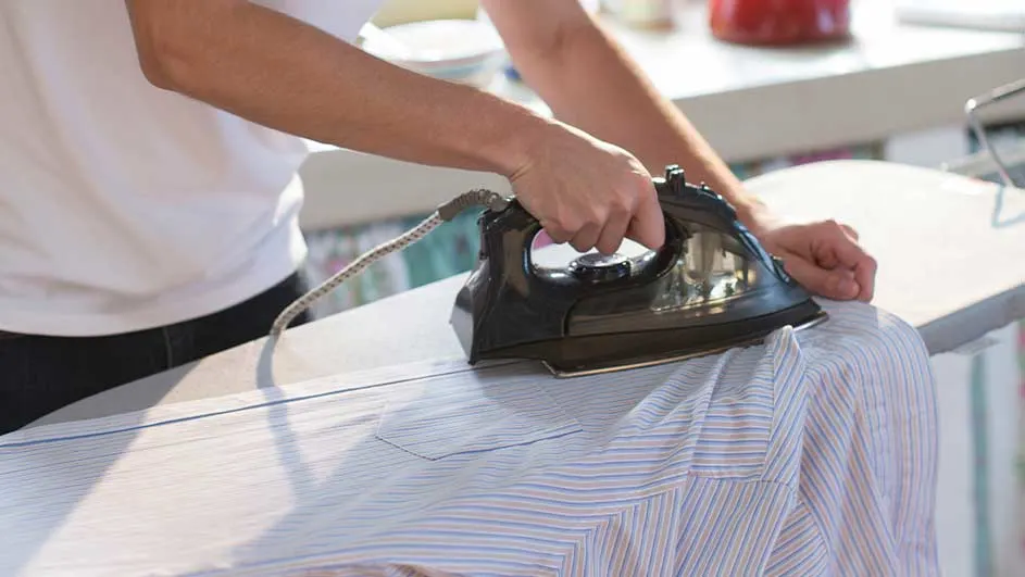 Une personne repasse une chemise rayée bleue et blanche sur une planche à repasser blanche avec un fer noir.
