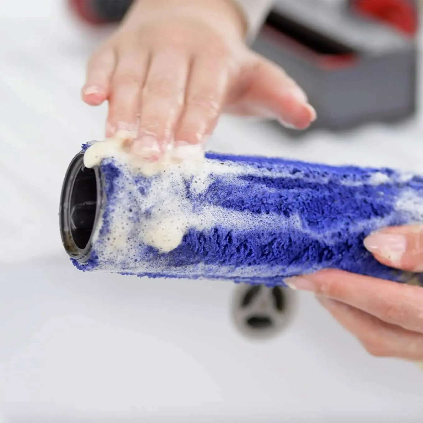 Une personne nettoie une brosse cylindrique bleue avec du savon blanc au-dessus d'un évier blanc.