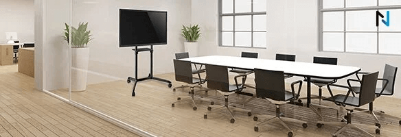 Vergaderruimte met witte tafel, zwarte stoelen en een zwart scherm op een rollende standaard. Er staan planten in witte potten.