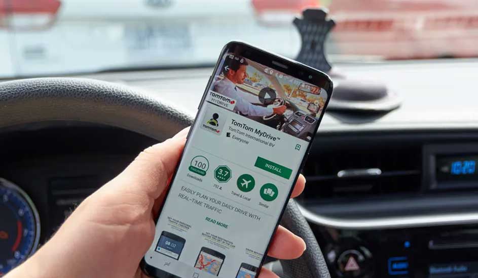 Zwarte smartphone toont TomTom MyDrive app in auto. Stuur en dashboard zijn zichtbaar. Het scherm toont een installatieknop.