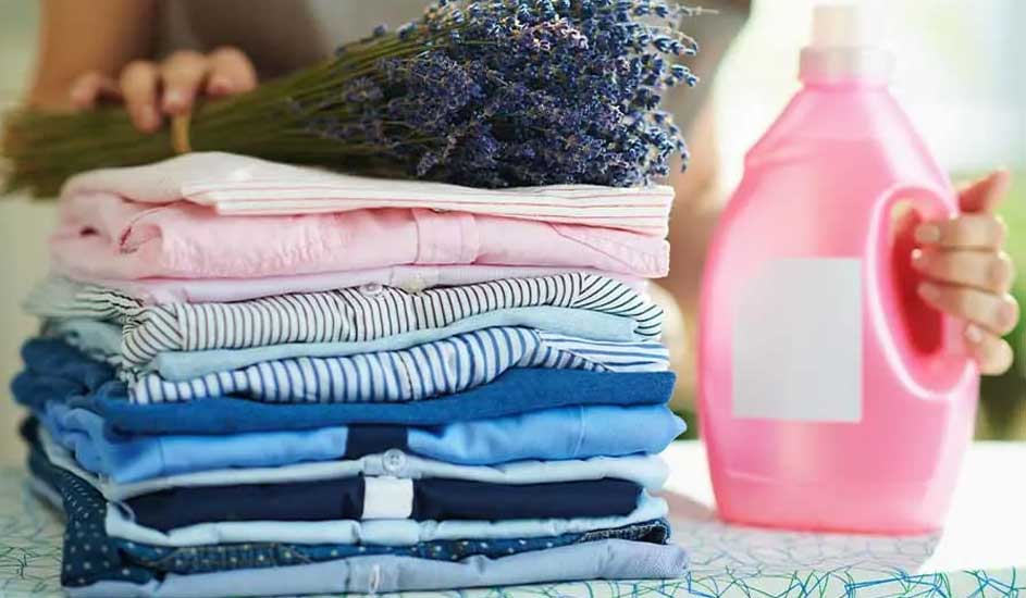Une pile de vêtements pliés, lavande et une bouteille de lessive rose sur une table à motifs.