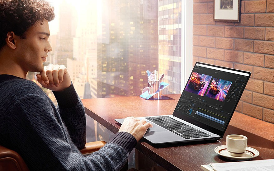 Een laptop staat op een bureau met een kop koffie ernaast, een stad is zichtbaar door het raam.