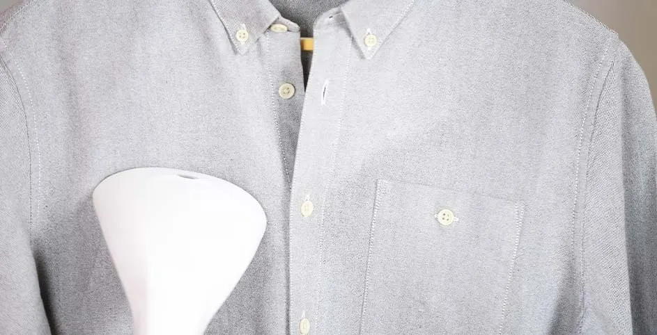 Un défroisseur blanc est utilisé sur une chemise boutonnée grise sur un cintre en bois.