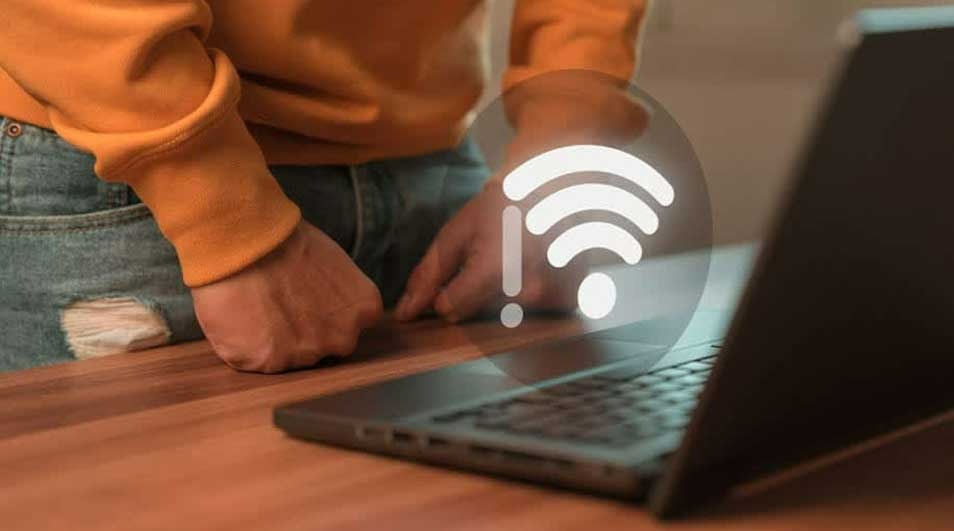 Une personne près d'un ordinateur portable noir sur une table en bois. Un symbole Wi-Fi blanc avec un point d'exclamation est visible.