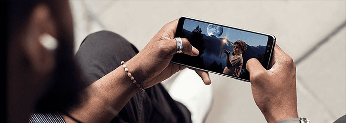 Gros plan sur un téléphone affichant une scène nocturne avec une lune et des montagnes. Les mains tiennent l'appareil sur un fond clair.