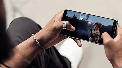 Persoon houdt een telefoon horizontaal vast. Het scherm toont een nachtscène met een volle maan en figuren.