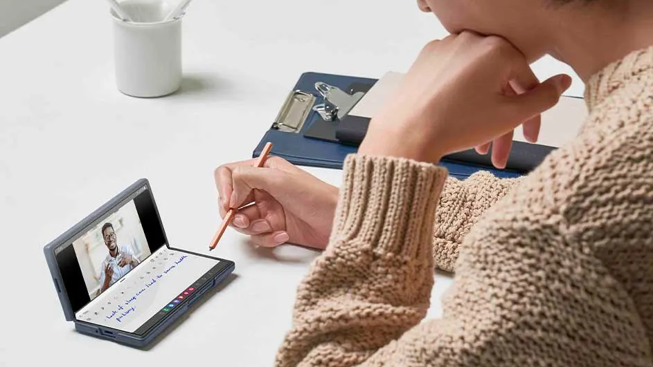 Tablet met video, hand met pen, klembord en witte beker op een witte tafel.