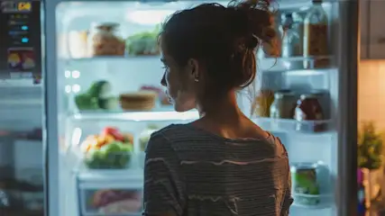 Une cuisine éclairée où un réfrigérateur ouvert expose des aliments variés sur plusieurs étagères.