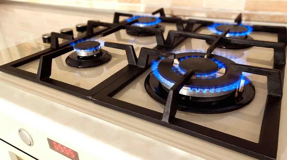Een close-up van een gasfornuis met vier branders aan. Blauwe vlammen branden onder zwarte pannenroosters op een licht aanrecht.