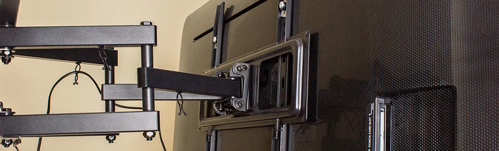 A black TV is mounted on a beige wall with an adjustable metal bracket. Cables are visible.