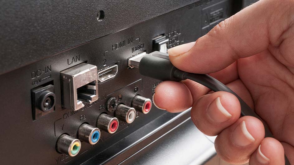 Une main connecte un câble HDMI noir à un port HDMI sur un téléviseur noir avec ports LAN, audio rouge, blanc et vert.