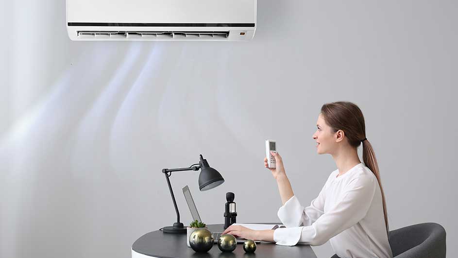 Un climatiseur blanc est installé au-dessus d'un bureau noir avec un ordinateur portable, une lampe et des décorations dorées.