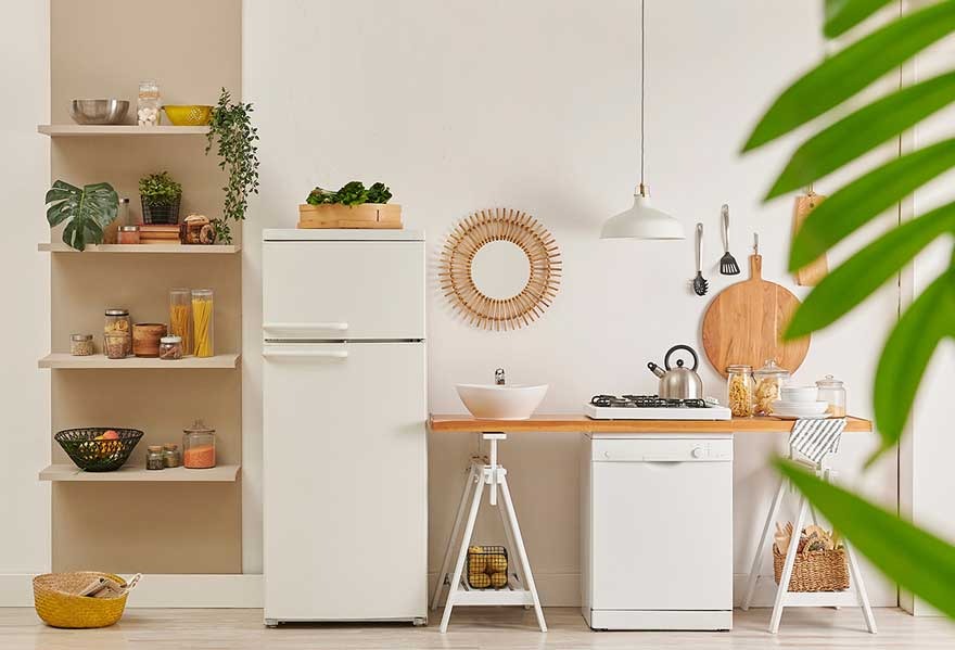 Witte keuken met houten plank, koelkast, vaatwasser en open schappen gevuld met keukengerei en planten. Decoratieve spiegel aan de muur.