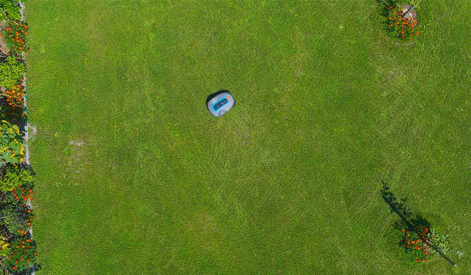 Een Gardena robotmaaier rijdt zelfstandig op een groot groen grasveld met bloemen aan de randen.