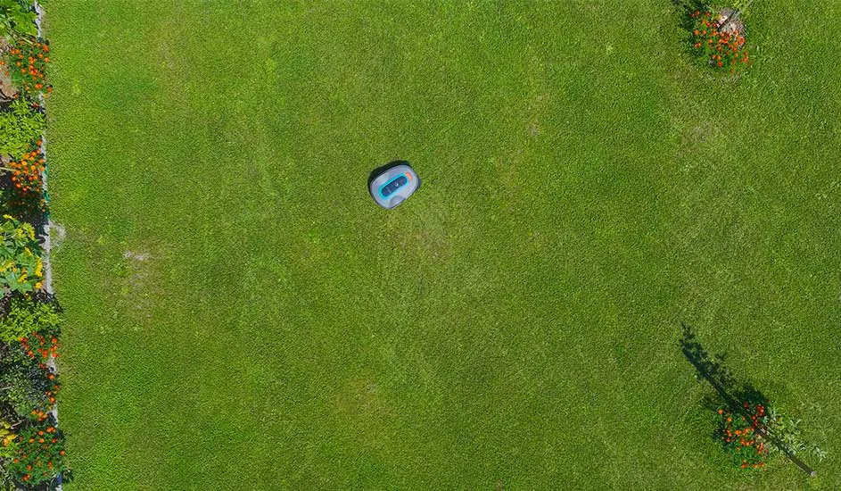 Een Gardena robotmaaier rijdt zelfstandig op een groot groen grasveld met bloemen aan de randen.